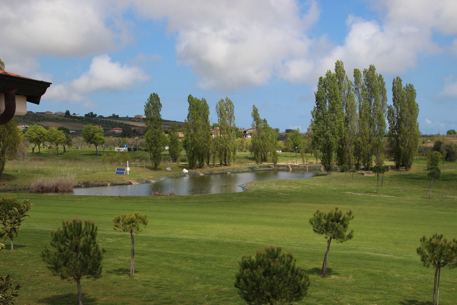 A golf course with a pond, trees, and a clear sky.