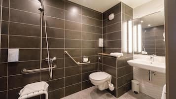 Une salle de bain moderne avec des carreaux de couleur sombre, une douche, des toilettes, un lavabo et une barre d’appui.