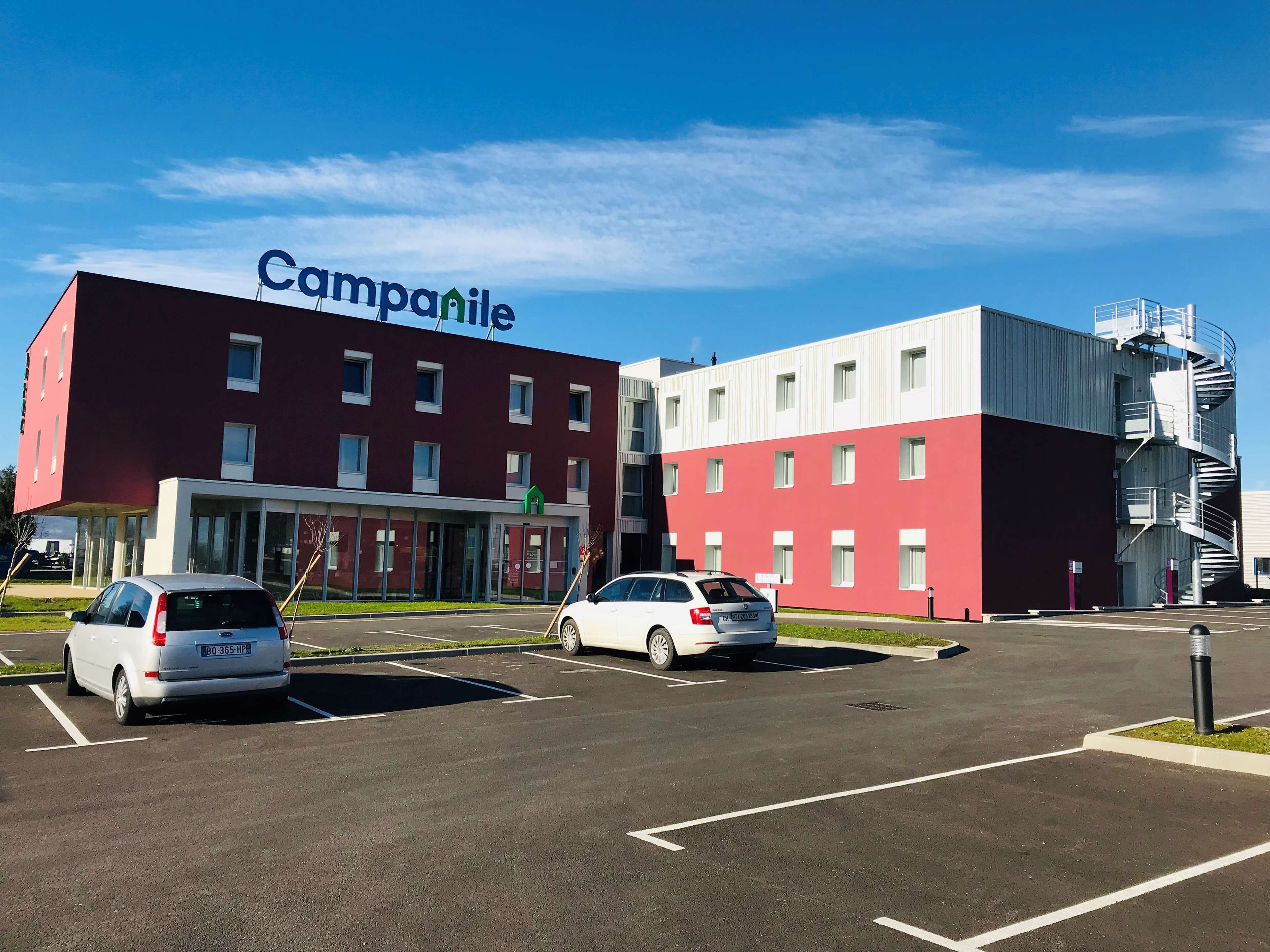 A modern building with a red and white facade, labeled "Campanile," featuring a parking lot with several cars.