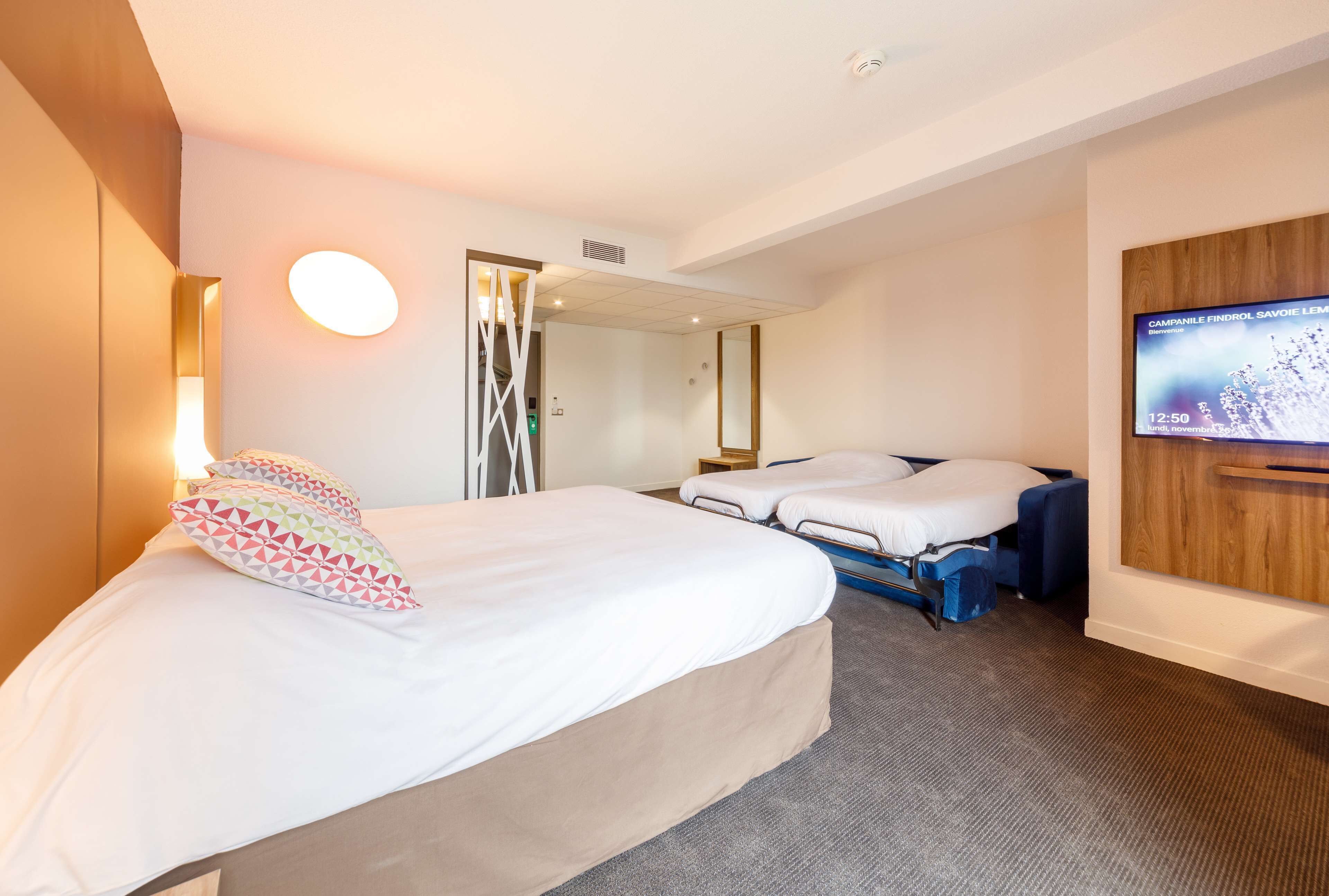 Una habitación de hotel con una cama grande, una cama más pequeña, un televisor en la pared y un espejo.