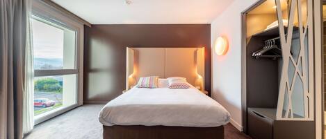 Una habitación de hotel moderna con una cama grande, un vestidor y vistas al exterior.