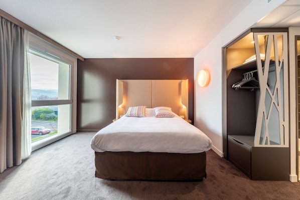 Una habitación de hotel moderna con una cama grande, un vestidor y vistas al exterior.