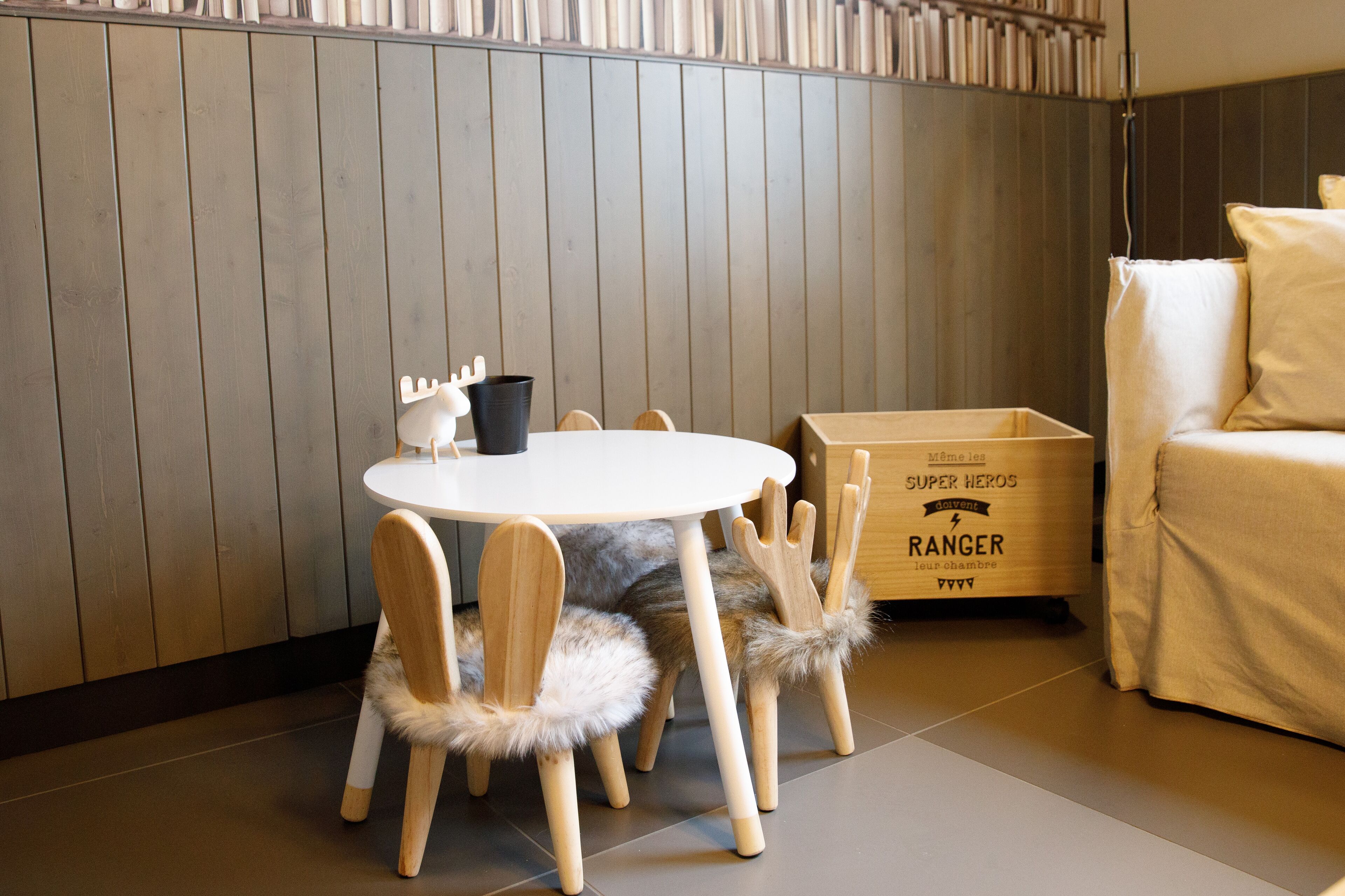 A room with a round table, wooden chairs with fur trim, a white sofa, and a wooden cabinet with text.