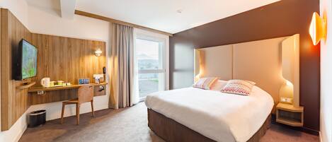 A hotel room with a large bed, a desk with a chair, a television, and a window with curtains.