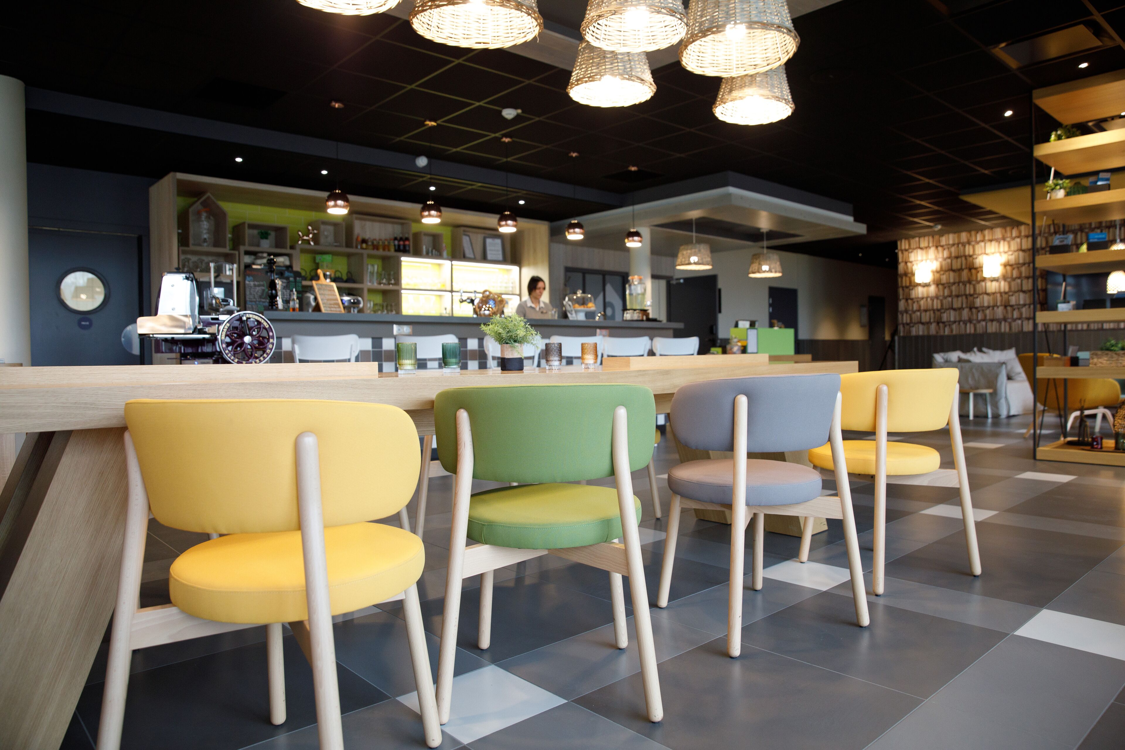 Un moderno interior de cafetería con una zona de bar, asientos de patas de madera e iluminación colgante.