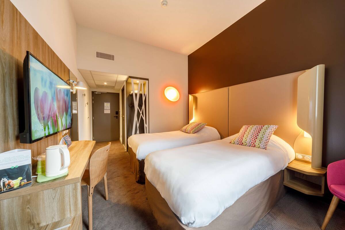A hotel room with two beds, a TV, a coffee maker, and a desk with a chair.