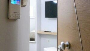 Et hotelværelse med en trædør, en termostat på væggen og et fjernsyn ophængt over en hylde.