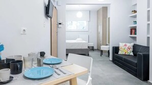 Et moderne, veloplyst rum med et spisebord dækket til to personer, en sort sofa med blomstermønstrede puder og en reol.