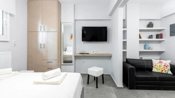 Et moderne hotelværelse med seng, skrivebord, sort sofa og fjernsyn.