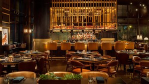 A modern restaurant with a bar area, leather seating, and a warm ambiance. - AC Hotel Austin-University (Austin)