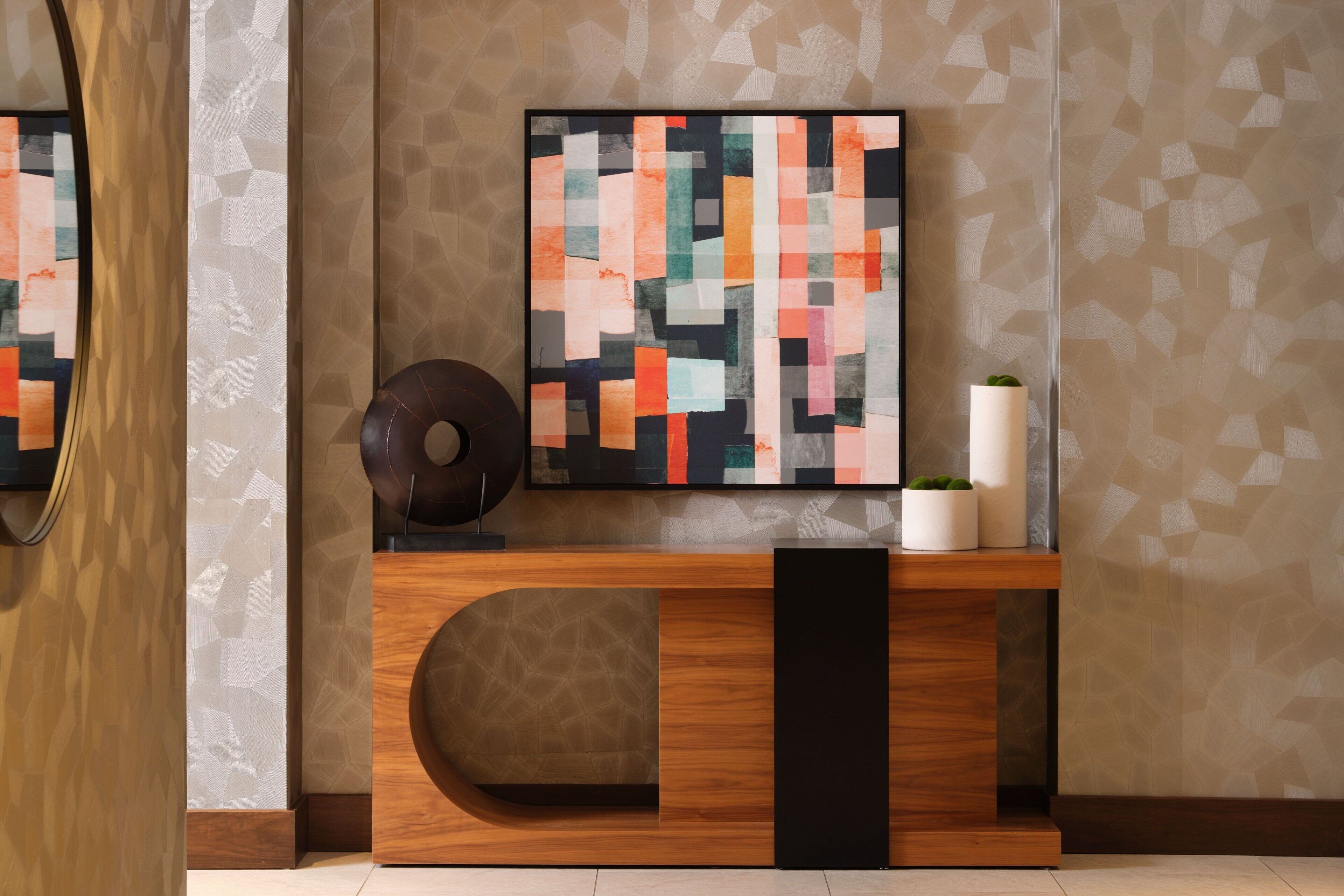 A modern reception area with a geometric-patterned wall, a wooden console table, and a colorful abstract painting.