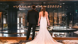 A couple standing in front of a large glass window with a view of a modern interior space. - AC Hotel Austin-University (Austin)
