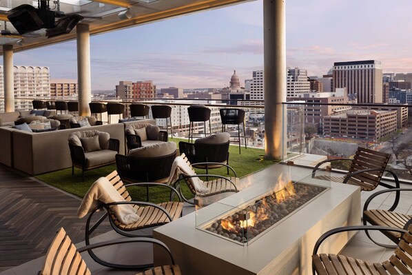 Un lounge en la azotea con chimenea, asientos al aire libre y vista panorámica de la ciudad.