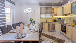 Une cuisine moderne avec un coin repas. Elle comprend un îlot de cuisine, une table à manger pour quatre personnes et une grande fenêtre avec des stores.