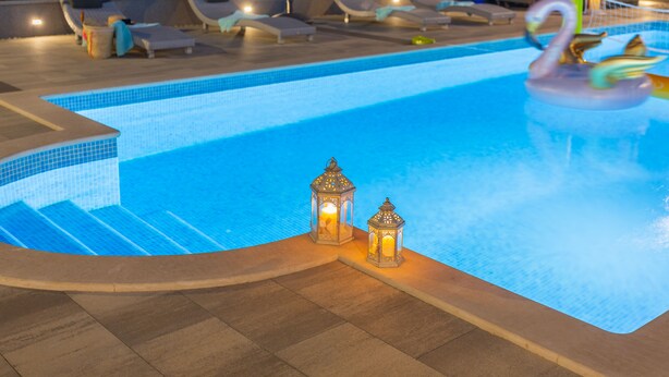 Une piscine avec des chaises longues et deux lanternes.