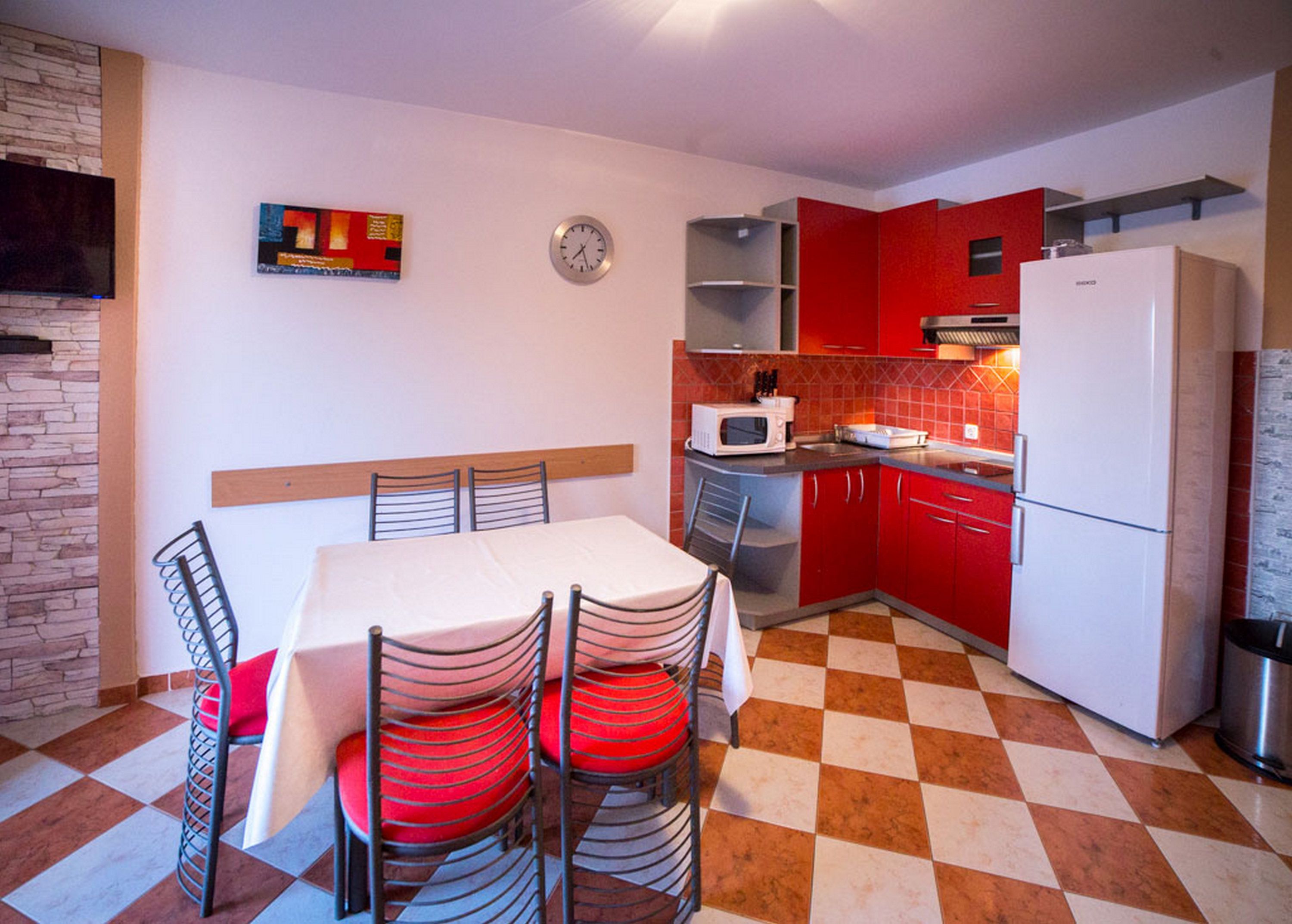A compact kitchen with a dining table, chairs, a microwave, and red cabinets.