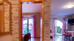 A room with a checkered floor, a stone wall, and a view through a doorway to a balcony with a table and chairs. - Apartment Sanic Rab 2 (Lopar)