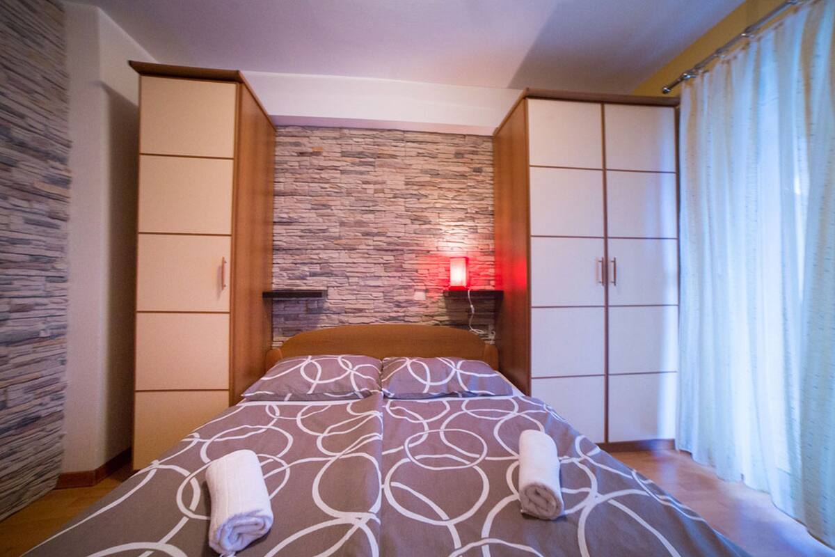 A bedroom with a bed, a stone wall, a red light, and a wooden wardrobe.