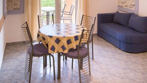 A dining area with a table and chairs, a blue sofa, a TV mounted on the wall, and a view through the glass doors. - Apartment Sanic Rab 2 (Lopar)