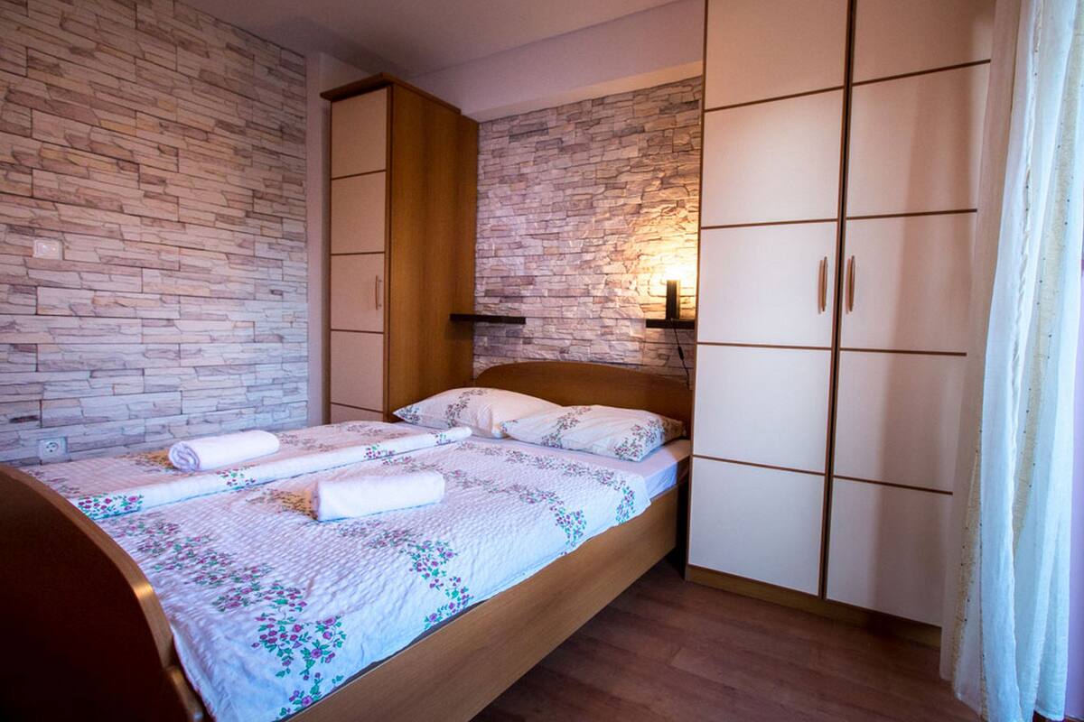 A bedroom with a wooden bed, a stone wall, and a wardrobe.