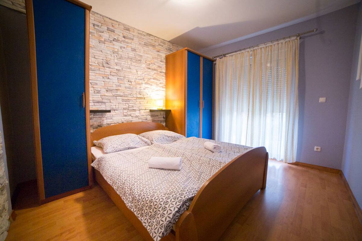 A bedroom with a bed, a stone wall, a wooden wardrobe, and a window with curtains.