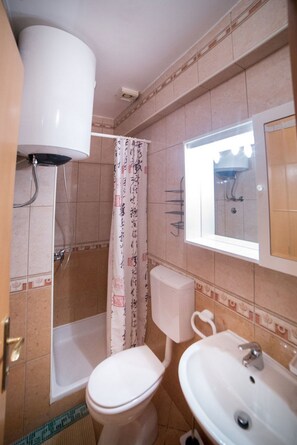Un baño con inodoro, lavabo, ducha y una ventana sobre el espejo.