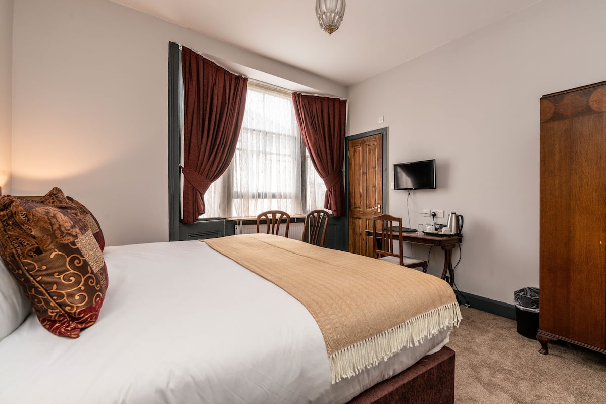 A hotel room with a large bed, a desk with a computer, a television, and a wardrobe.