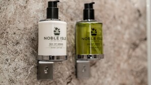 Two hand lotion bottles labeled 'Noble Isle' on a textured wall.