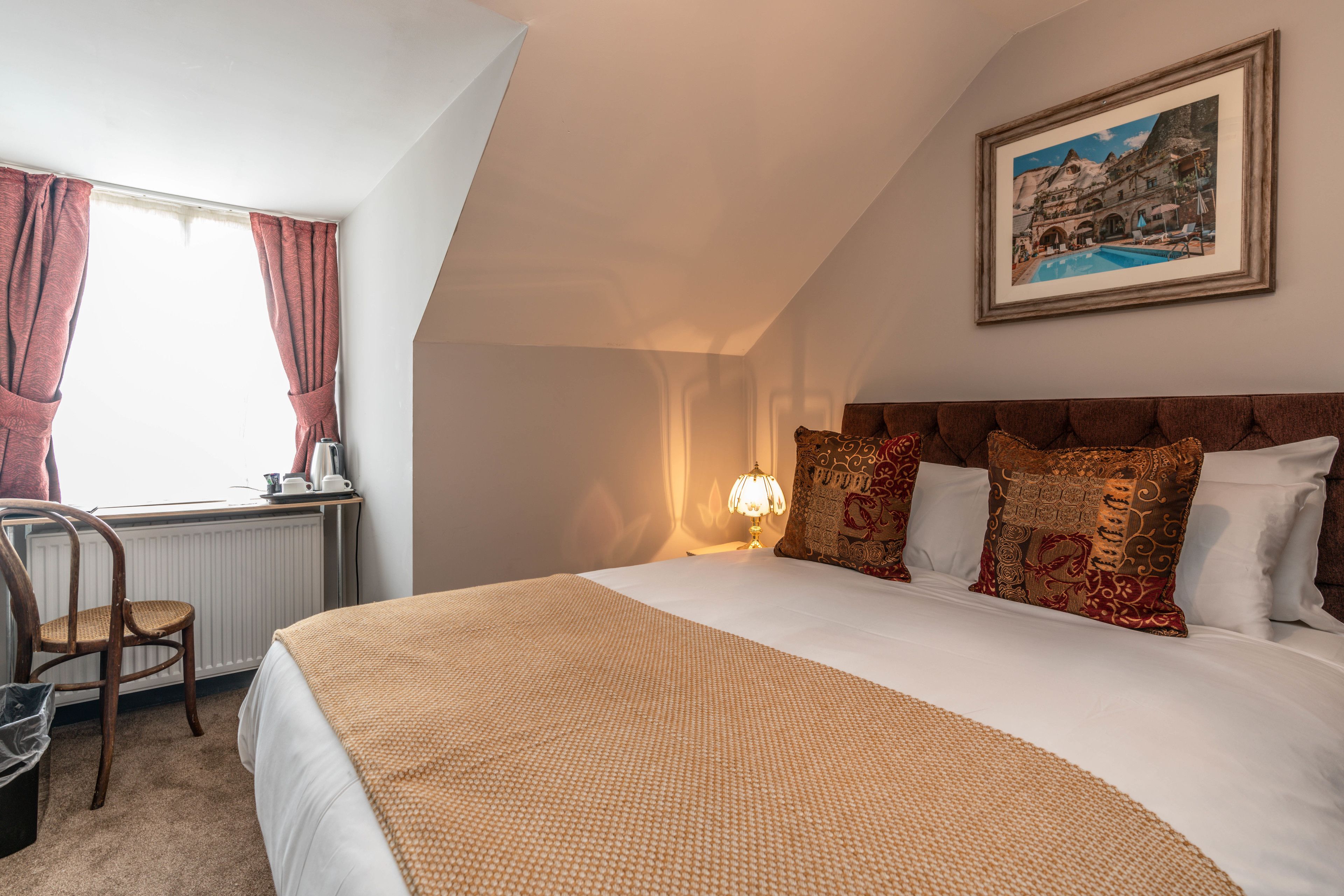 A bedroom with a large bed, a desk with a chair, a radiator, and a framed picture on the wall.