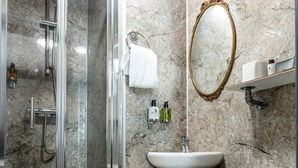 A bathroom with a glass-enclosed shower, a white sink, a toilet, and a marble wall.