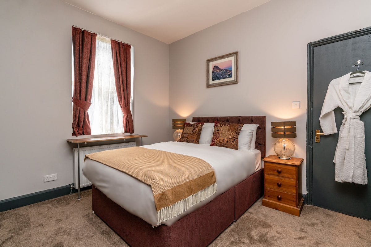 A bedroom with a bed, bedside table, lamp, and a robe hanging on the door.
