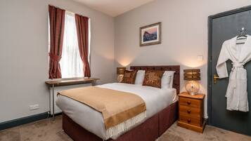 A bedroom with a bed, bedside table, lamp, and a robe hanging on the door.