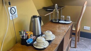 A kitchenette with a coffee maker, two cups, and a bottle on the counter.