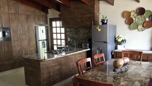 Une cuisine avec des meubles de rangement en bois foncé, un réfrigérateur en acier inoxydable, une cuisinière à gaz et un plan de travail en marbre.
