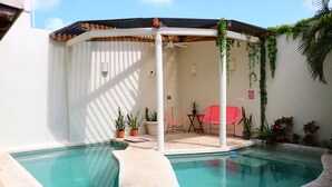 Un espace piscine comprenant deux piscines, un coin salon couvert avec des chaises et des plantes en pot.