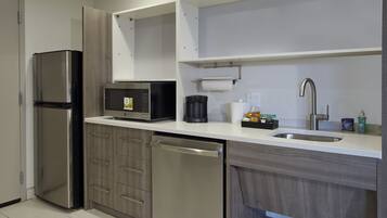 A compact kitchen with a stainless steel refrigerator, a microwave, a dishwasher, a sink, and a coffee maker.