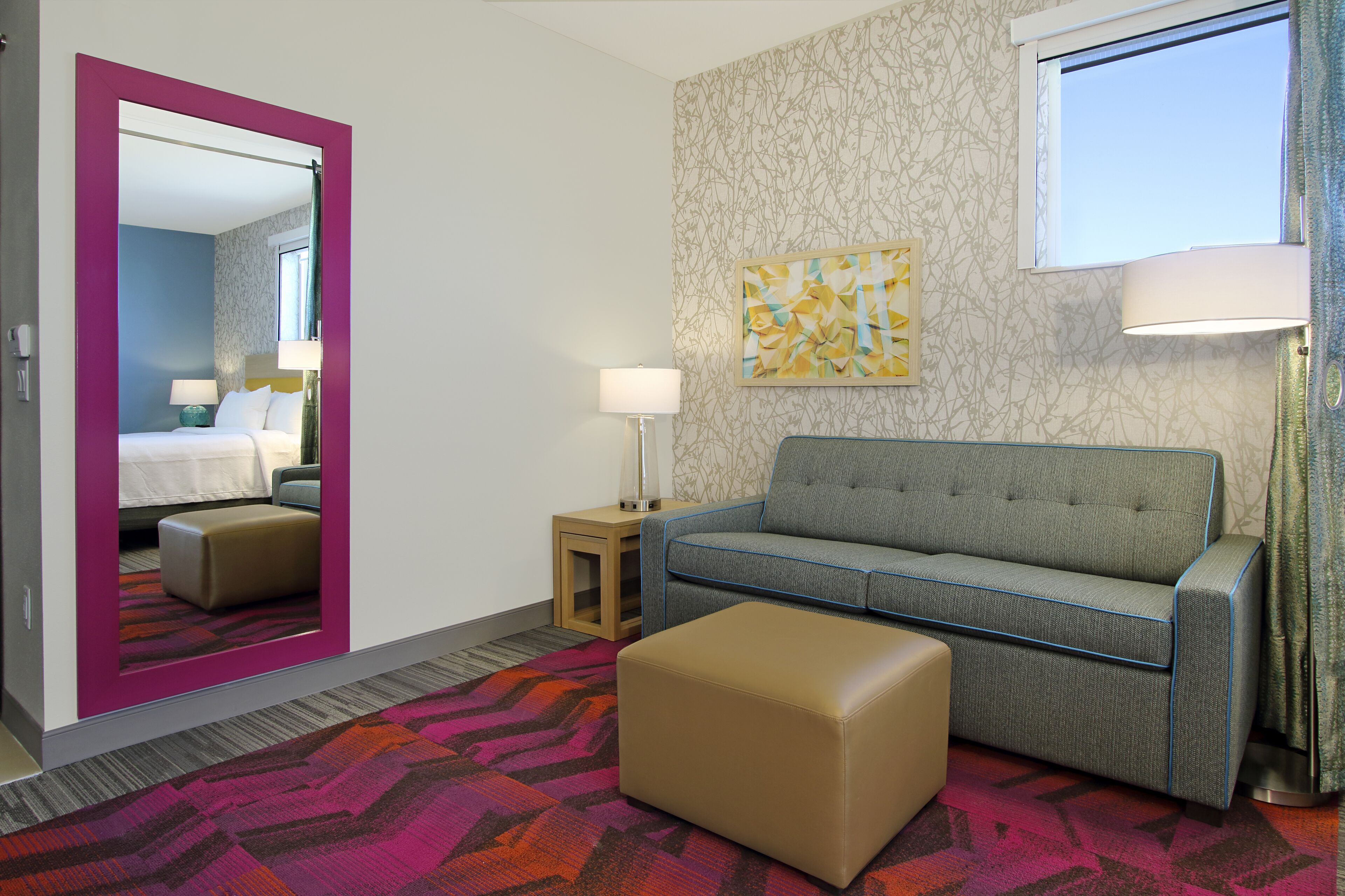 Une chambre d’hôtel avec un lit, un canapé, une petite table, une lampe et un tapis coloré.