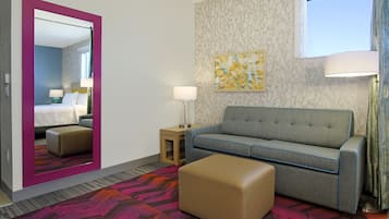Une chambre d’hôtel avec un lit, un canapé, une petite table, une lampe et un tapis coloré.