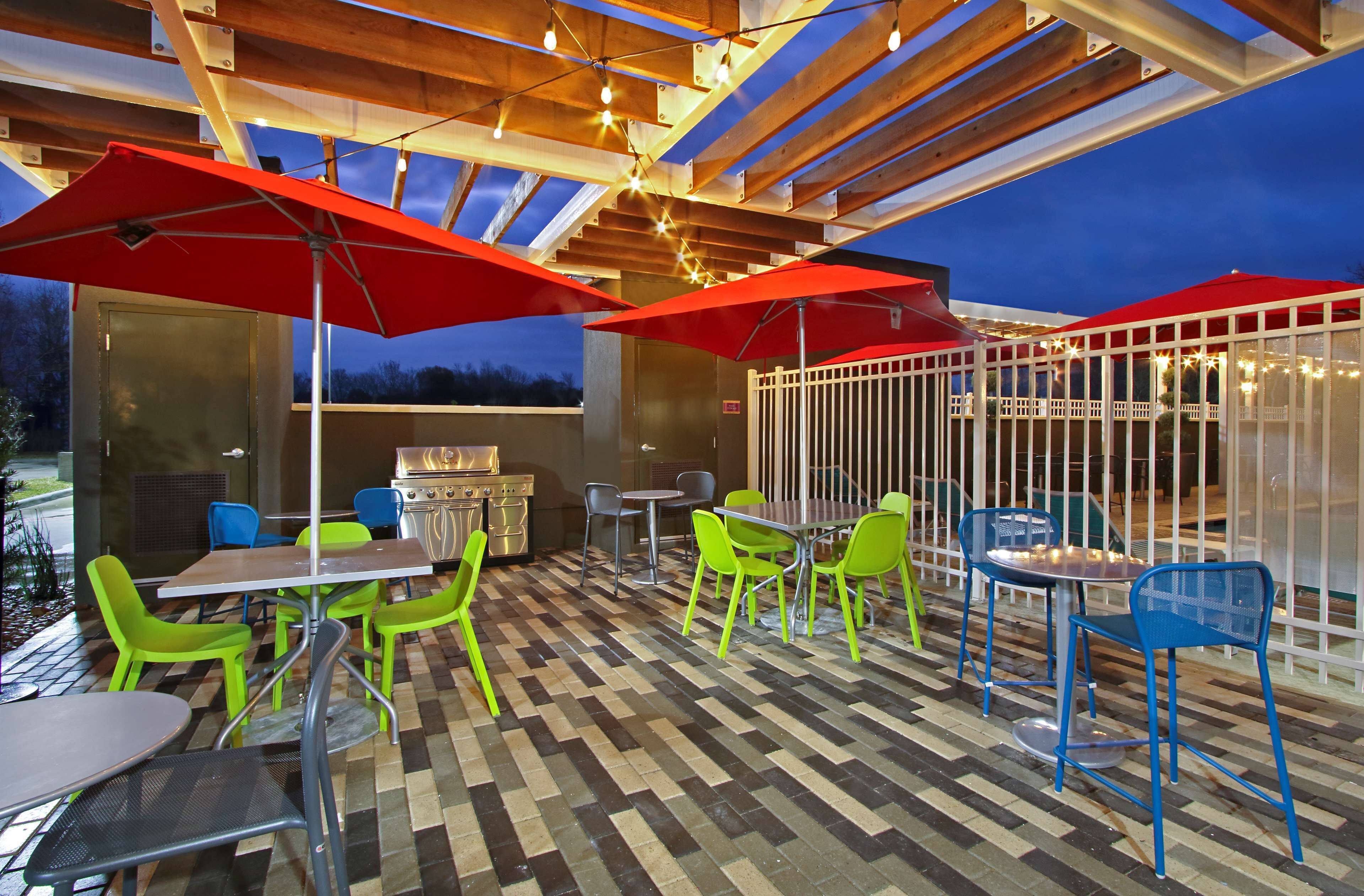 Une terrasse extérieure avec des tables et des chaises, des parasols rouges et des guirlandes lumineuses.