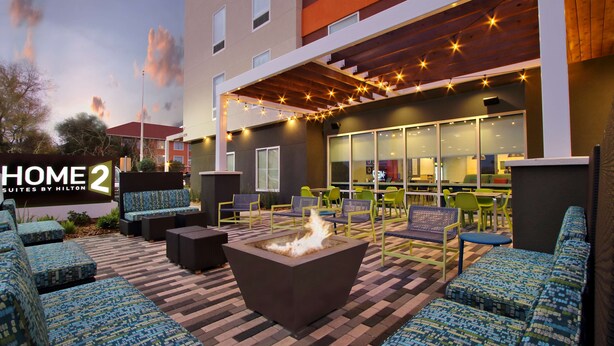 A hotel patio with outdoor seating, a fire pit, and a modern building facade. - Home2 Suites by Hilton Beaumont (Beaumont)