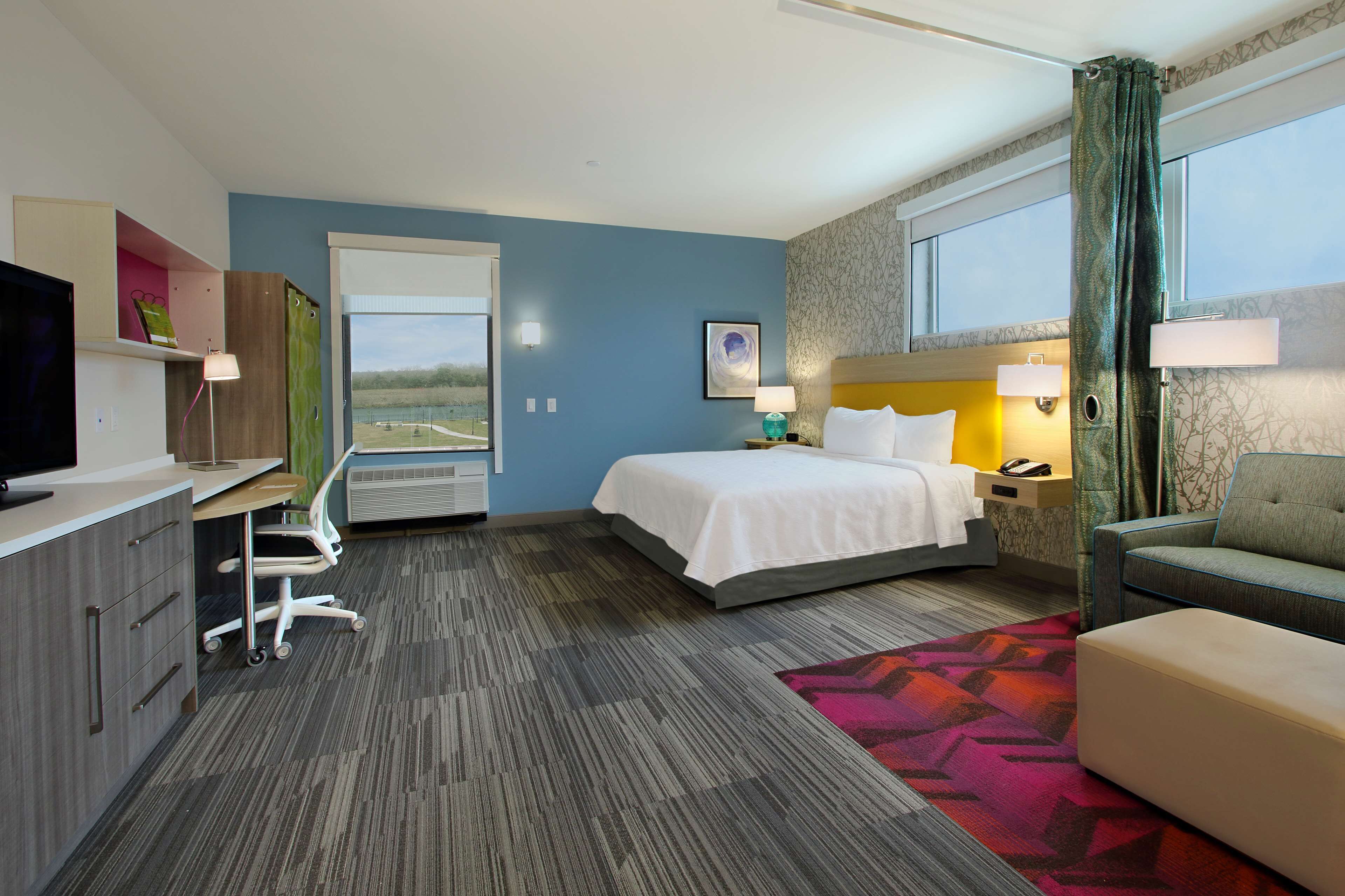 A hotel room with a bed, desk, chair, and a TV.