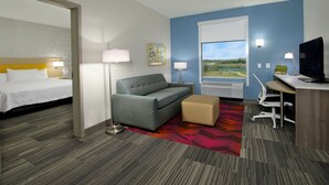 A hotel room with a bed, a sofa, a desk, and a window with a view. - Home2 Suites by Hilton Beaumont (Beaumont)