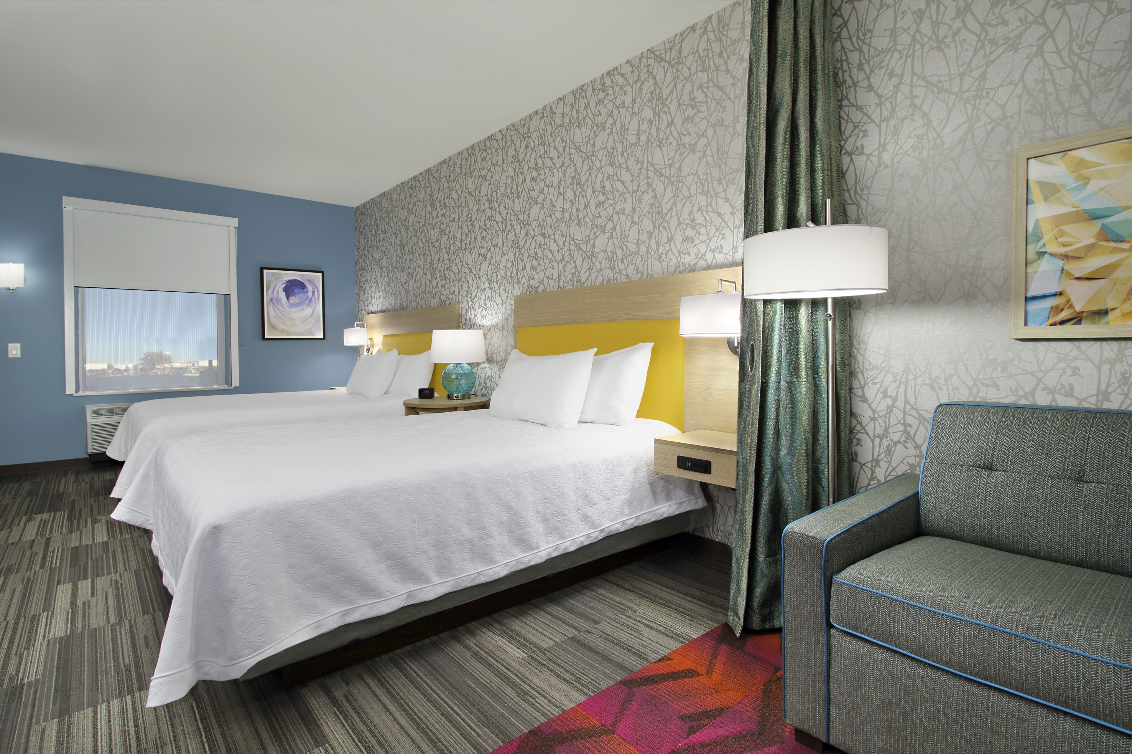 A hotel room with a large bed, two bedside tables, a chair, and a view of the city through the window.