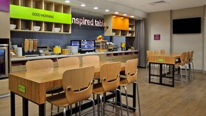 A restaurant with multiple tables and chairs, a counter with food items, and a 'GOOD MORNING' sign. - Home2 Suites by Hilton Beaumont (Beaumont)