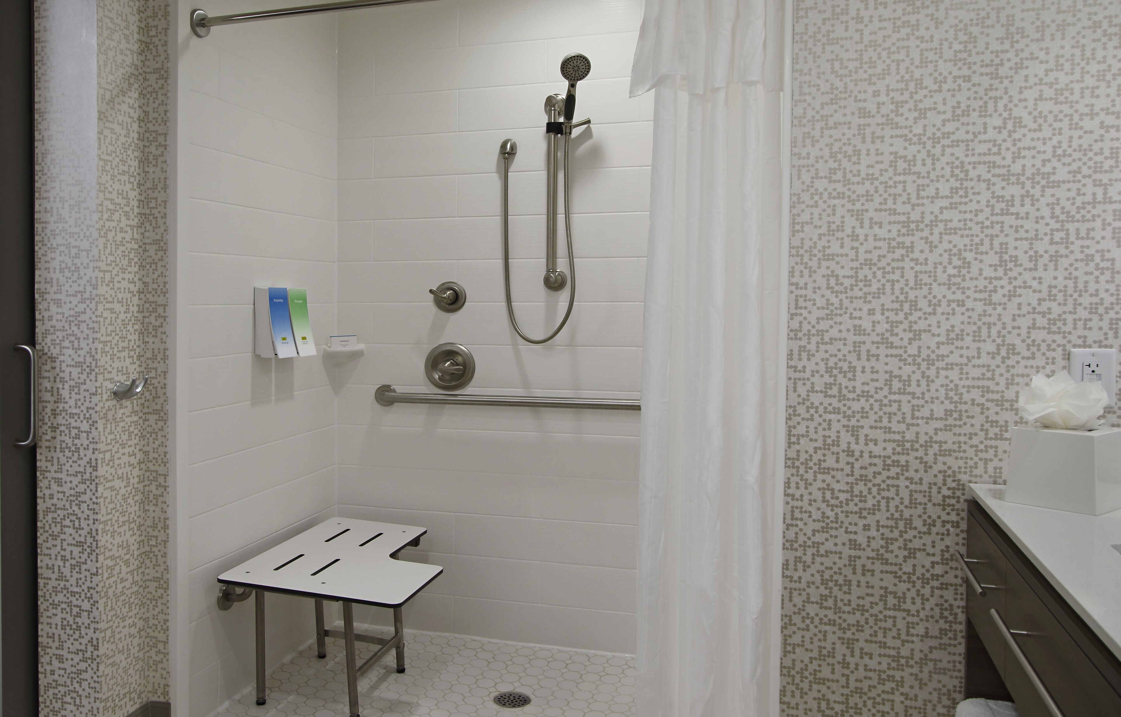 A shower area with a handheld showerhead, a towel rack, and a small table.
