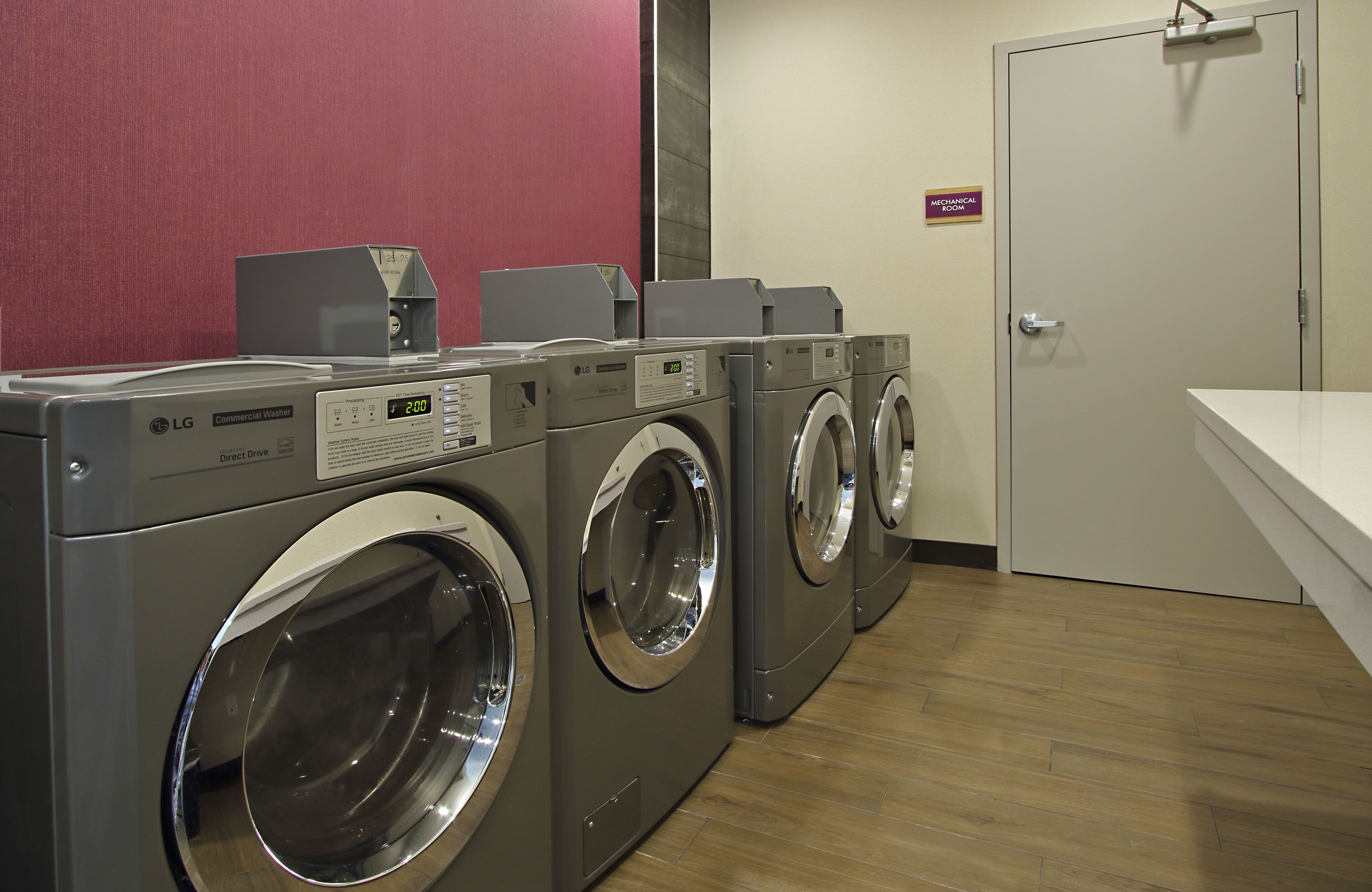A laundry facility with three LG commercial washers and dryers, a wooden floor, and a sign indicating a mechanical room.