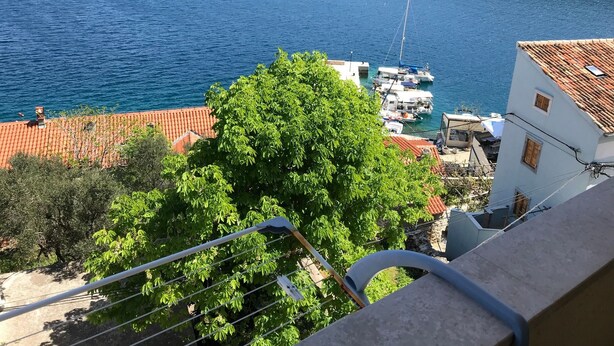 A coastal view with a clear blue sea, a dock with boats, and a building with a red-tiled roof. - Apartments Tarcizio (Cres)