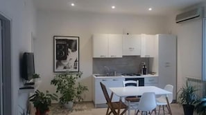 A modern kitchen with white cabinets, a dining table with chairs, and a potted plant. - Palermo Inn (Palermo)