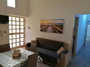 A living room with a sofa, a table with a tray, and a painting of a sunset over a beach. - Palermo Inn (Palermo)