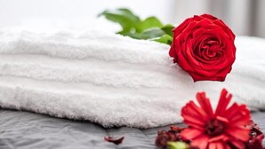 Une serviette blanche, soigneusement pliée, ornée d’une rose rouge et de fleurs rouges, le tout posé sur une surface texturée.